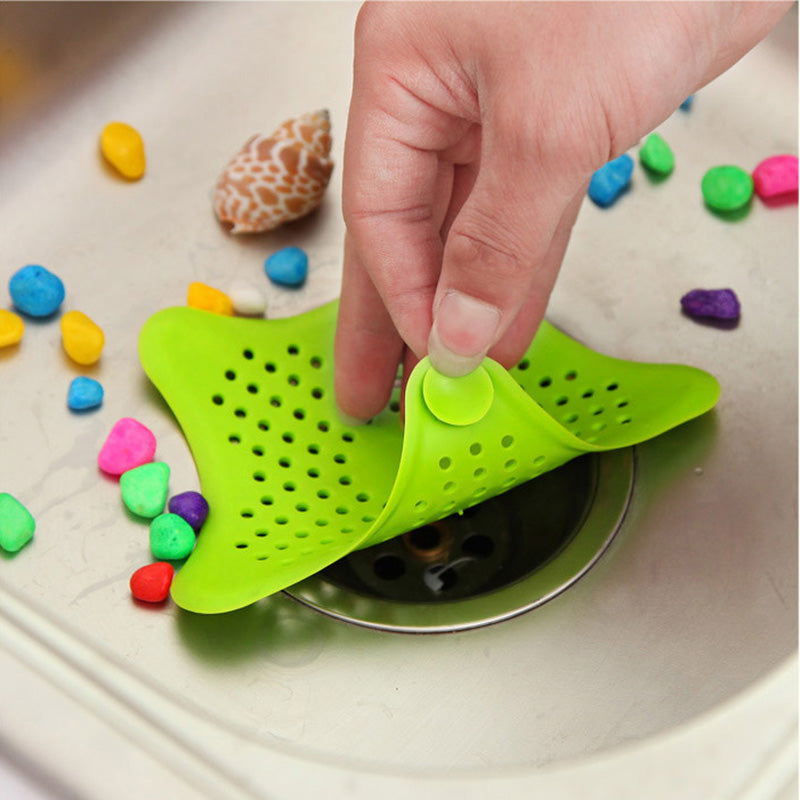 Green silicone drain cover being placed over a sink drain with colorful bath bombs around.